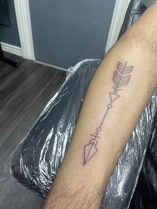 Tatuaje de fuerza y superación de una flecha en el antebrazo