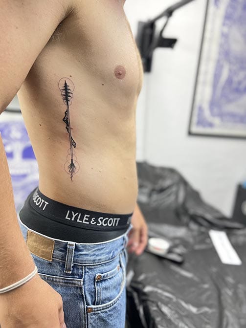 Tatuaje minimalista para hombre con significado, flecha, montañas y naturaleza en las costillas