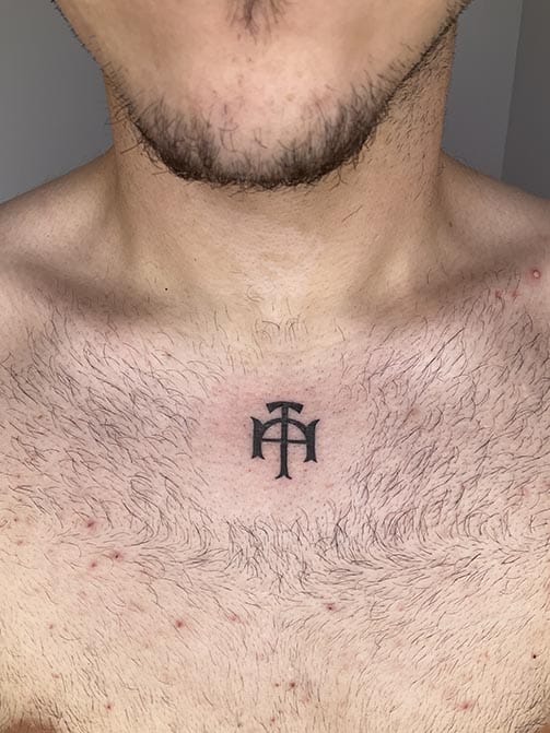 Tatuaje pequeño para hombre de una cruz o simbolofamiliar en el pecho