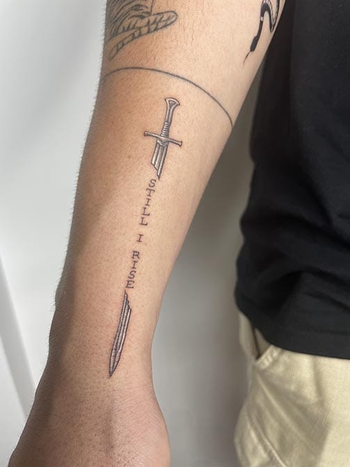 Tatuaje pequeño para hombre en el antebrazo de una espada con una frase