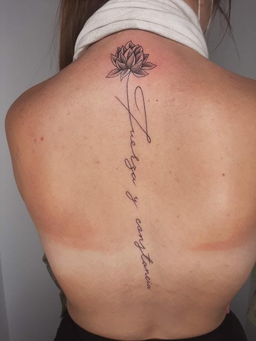 Tatuaje en la columna para mujer de una frase en la espalda con una flor de loto