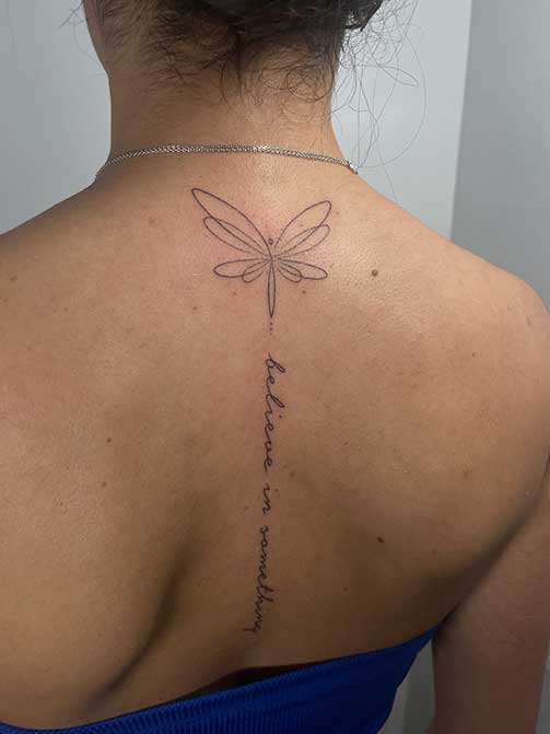 Tatuaje en la columna para mujer de una frase en la espalda con una libélula