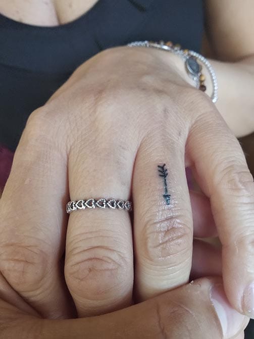 Tatuaje minimalista femenino de una flecha pequeña para mujer en el dedo