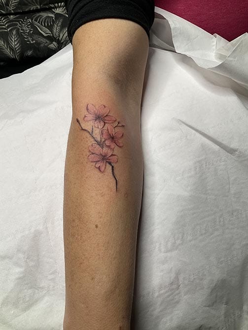 Tatuaje minimalista femenino de flores de almendro pequeñas a color para mujer en el antebrazo