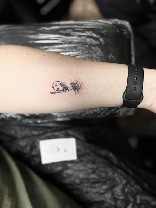 Tatuaje minimalista femenino de una mariquita pequeña para mujer en el brazo