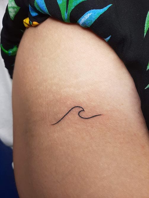 Tatuaje minimalista femenino de una ola pequeña para mujer en el muslo