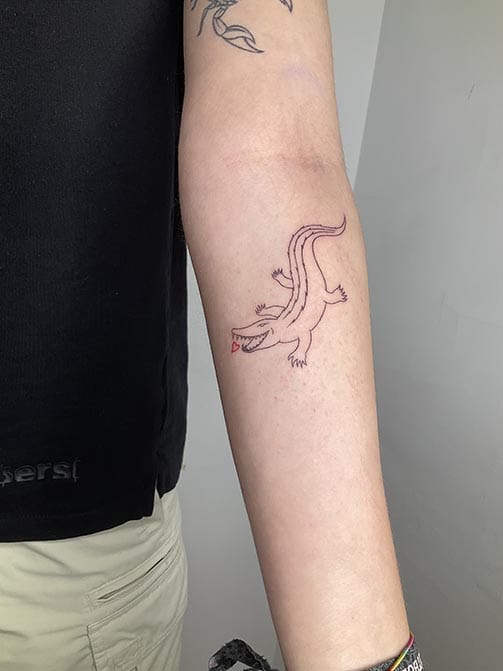 Tatuaje estilo fine line de un cocodrilo con un corazón en el brazo