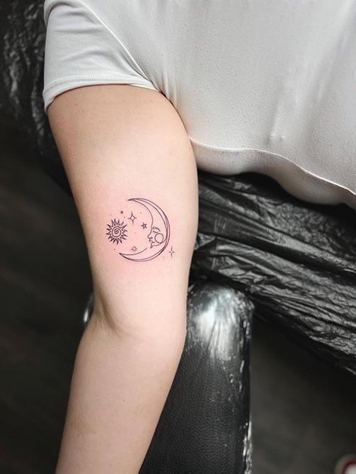 Tatuaje estilo fine line de una luna con estrellas en el brazo