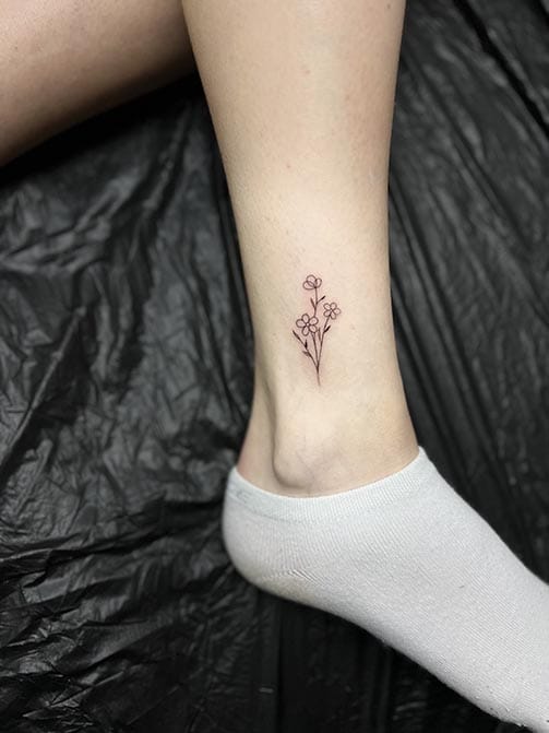 Tatuaje estilo fine line de flores en el tobillo
