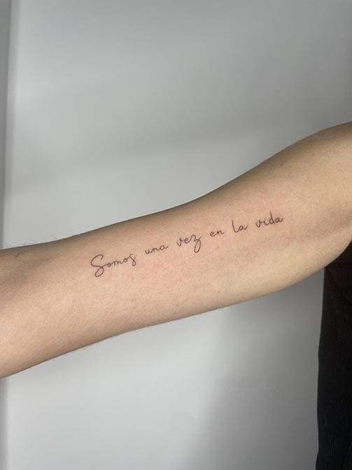 Tatuaje estilo fine line de una frase en el brazo