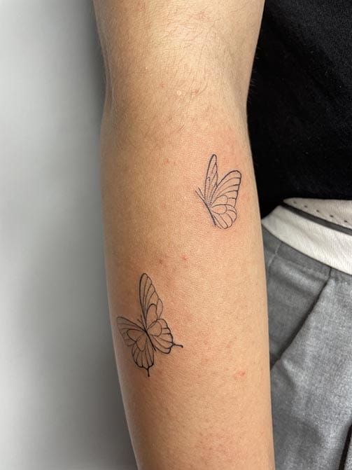Tatuaje estilo fine line de dos mariposas volando en el antebrazo
