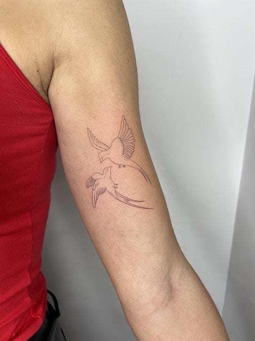 Tatuaje estilo fine line de dos golondrinas volando en el brazo
