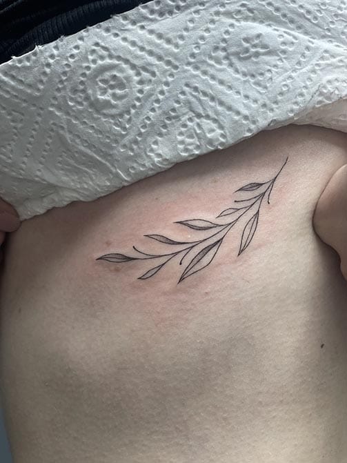 Tatuaje estilo fine line de una rama con hojas