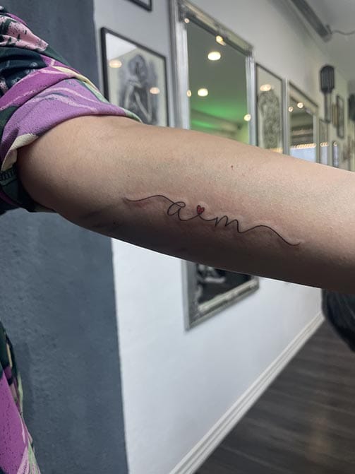 Tatuaje de iniciales de seres queridos entrelazados por un corazón en el brazo