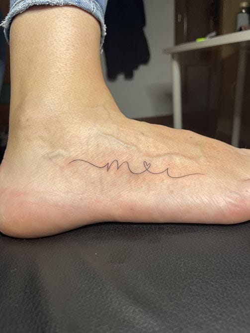 Tatuaje de iniciales de seres queridos entrelazados por un corazón en el pie