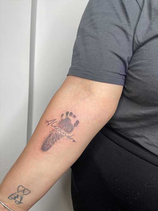 Tatuaje de la huella de un hijo con su nombre en el antebrazo