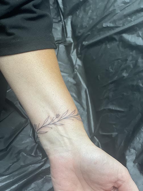 Tatuaje pequeño para mujer en el brazo de una pulsera de temática botánica de ramas
