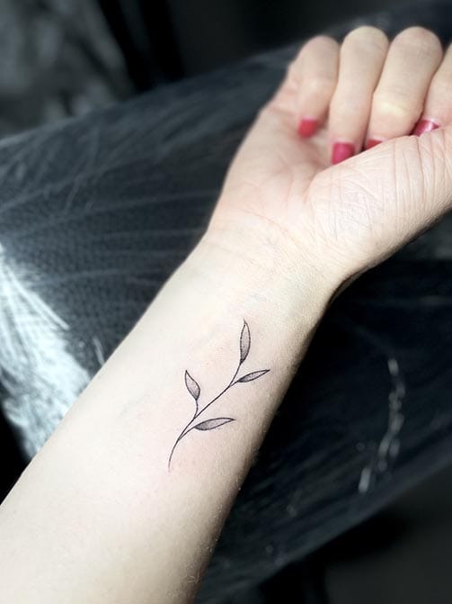 Tatuaje pequeño para mujer en el brazo de temática botánica de una rama
