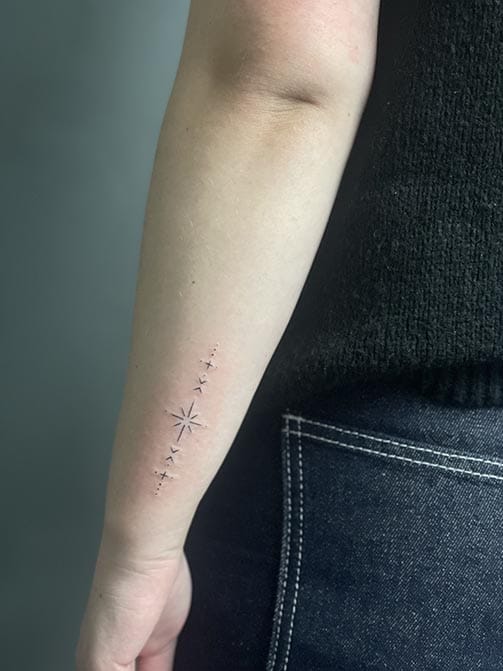 Tatuaje pequeño para mujer en el brazo con símbolos y estrellas